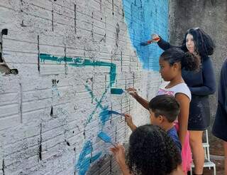 Artistas visual ajudando crainaças a pintar muro (Foto: Divulgação)