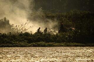 Brigadistas quase desaparecem em meio a fumaça do outro lado da margem do rio (Foto: Guilherme Giovanni)