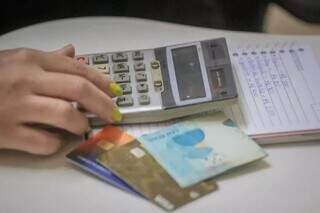 Mulher com cartões e nota faz contas na calculadora (Foto: Marcos Maluf)