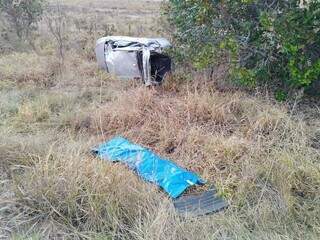 Carro destruído em vegetação e corpo da vítima coberto. (Foto: Campo Grande News)