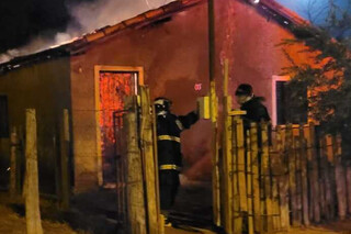 Casa destruída por incêndio e bombeiros no combate ao fogo. (Foto: Divulgação)