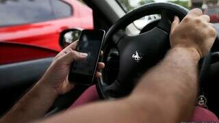 Homem manuseia celular com mão no volante. (Foto: Marcelo Camargo/Agência Brasil)