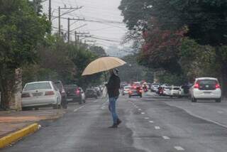 Pedestre segurando guarda-chuva enquanto atravessa a rua na região central na última quinta-feira (Foto: Juliano Almeida)