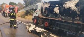 Caminhão destruído por incêndio e bombeiros no combate ao fogo. (Foto: Campo Grande News)