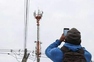 Homem com celular próximo à torre de distribuição de sinal (Foto: Henrique Kawaminami)