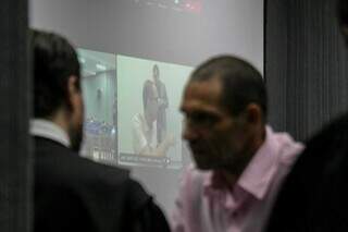 De camisa rosa, Marcelo Rios conversa com advogado enquanto Jamil Name Filho, que acompanha por videoconferência, tem imagem projetada em telão (Foto: Henrique Kawaminami)