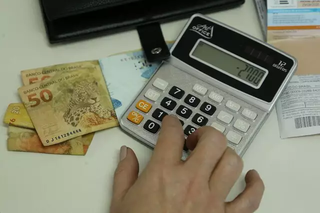 Mulher fazendo contas na calculadora, com dinheiro ao lado. (Foto: Arquivo/Campo Grande News)