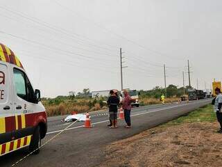 Corpo da vítima coberto por lençol no meio da pista e local isolado (Foto: Geniffer Valeriano)