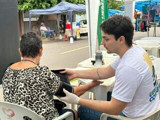 Acadêmico aferindo pressão de idosa na feira (Foto: Marcos Maluf)