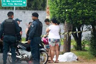 Corpo da vítima coberto com lençol branco e ao lado policiais militares e a família do homem (Foto: Henrique Kawaminami)