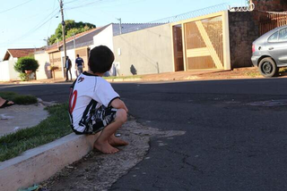 Criança sentada na calçada observando a rua. (Foto: Arquivo/Campo Grande News)