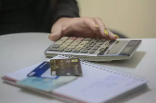 Consumidora fazendo conta na calculadora com gastos anotados em caderno (Foto: Marcos Maluf)