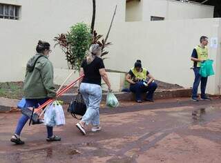 Mulher carregando duas vassouras e um rodo, que usou para limpar o túmulo (Foto: Osmar Veiga)