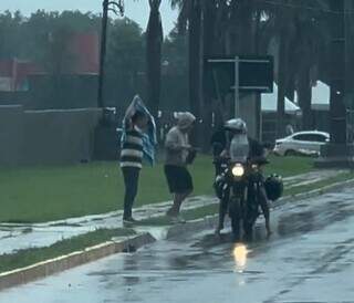 Deputado estadual Lídio Lopes se protege com toalha e ajuda o filho a chegar ao local de prova do Enem (Foto: Reprodução)