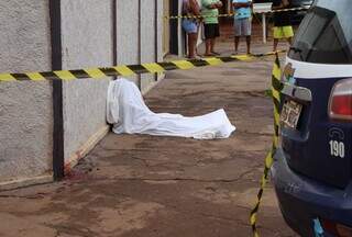 Corpo da vítima escorado no muro de uma casa e coberto com um lençol branco (Foto: Osmar Veiga)