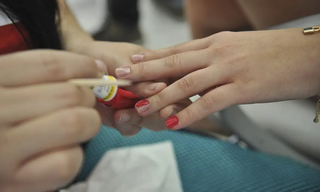 Profissional de beleza aplica esmalte vermelho na mão de cliente. (Foto: Elza Fiúza/Agência Brasil)