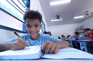 Estudante sorri, em uma sala de aula onde todos usam o uniforme azul da Reme (Foto: Divulgação Semed)