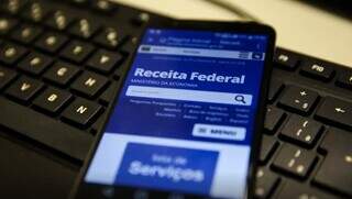 Smartphone com acesso ao site da Receita Federal sobre teclado de computador (Foto: Marcelo Casal Jr./Agência Brasil)