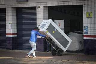 Trabalhador carregando geladeira para dentro de loja, em Campo Grande (Foto: Marcos Maluf)