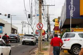 Pedestre caminha na calçada próximo aos fios soltos. (Foto: Henrique Kawaminami)