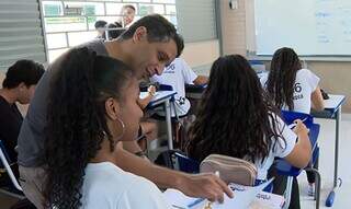 Professor ajuda estudante com conteúdo em sala de aula (Foto: TV Brasil)