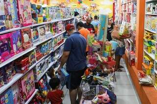 Pais escolhendo brinquedos em loja de Campo Grande; preço dos produtos ajudam no aumento da inflação (Foto: Henrique Kawaminami)