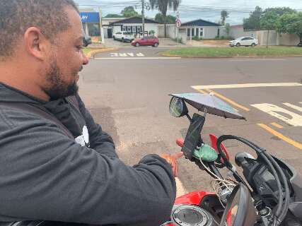 Motoetregador roda cidade com mini guarda-chuva protegendo celular