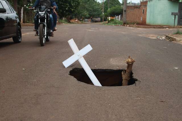 Moradores improvisam cruz para sinalizar buraco em rua do Jardim Centenário
