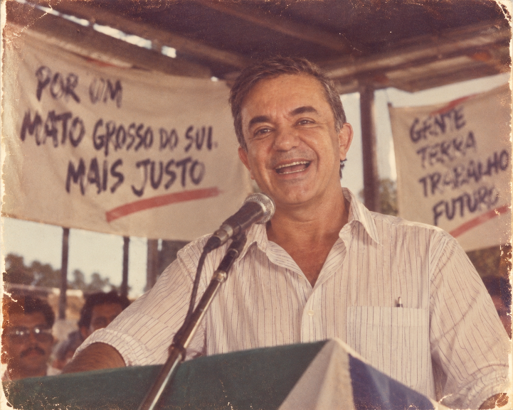 Vander Loubet – Vander aparece em um palanque à moda antiga, com microfone com fio, camisa social e faixas pintadas à mão.