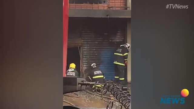 Bombeiro tenta serrar porta de loja enquanto equipe continua no combate ao fogo